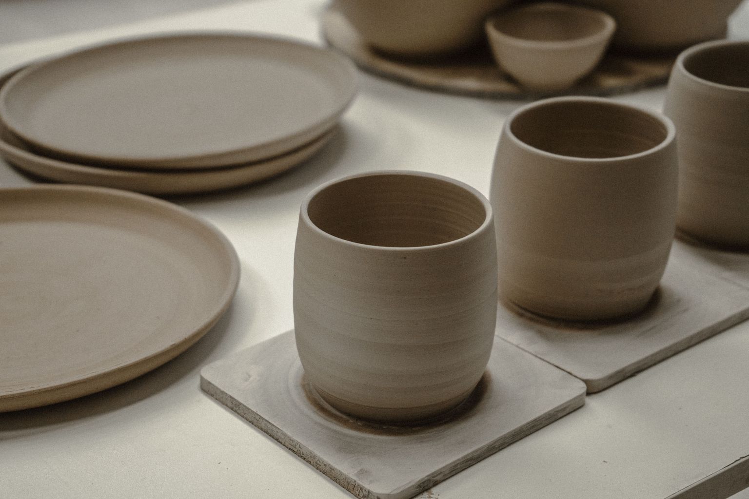 Unglazed cups and plates on a studio table in daylight.