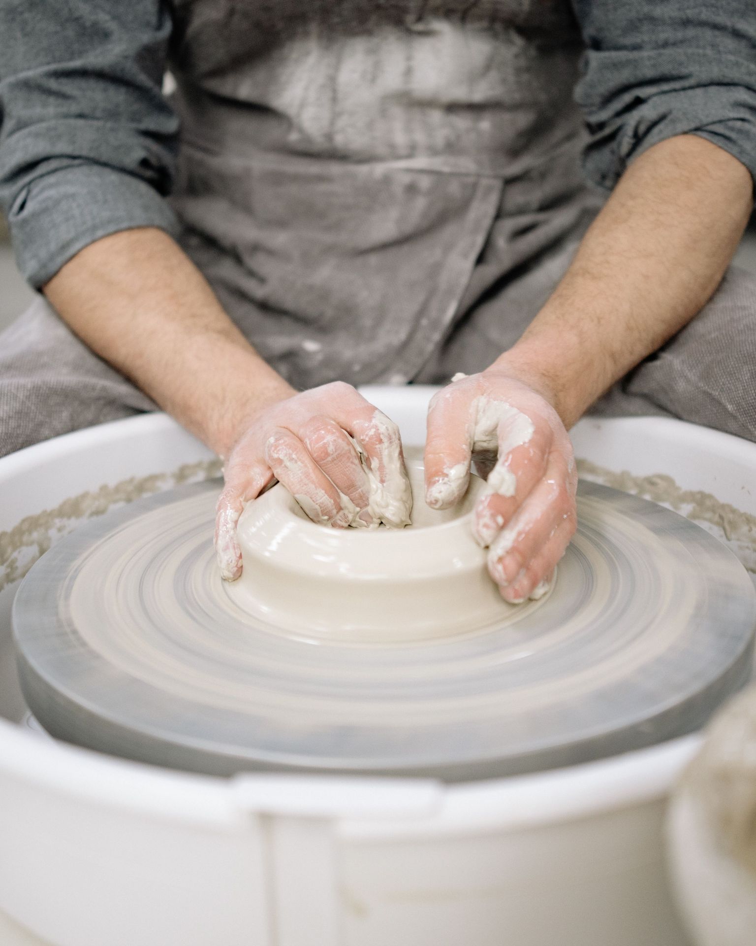 Hands centring the clay on the wheel and opening it.