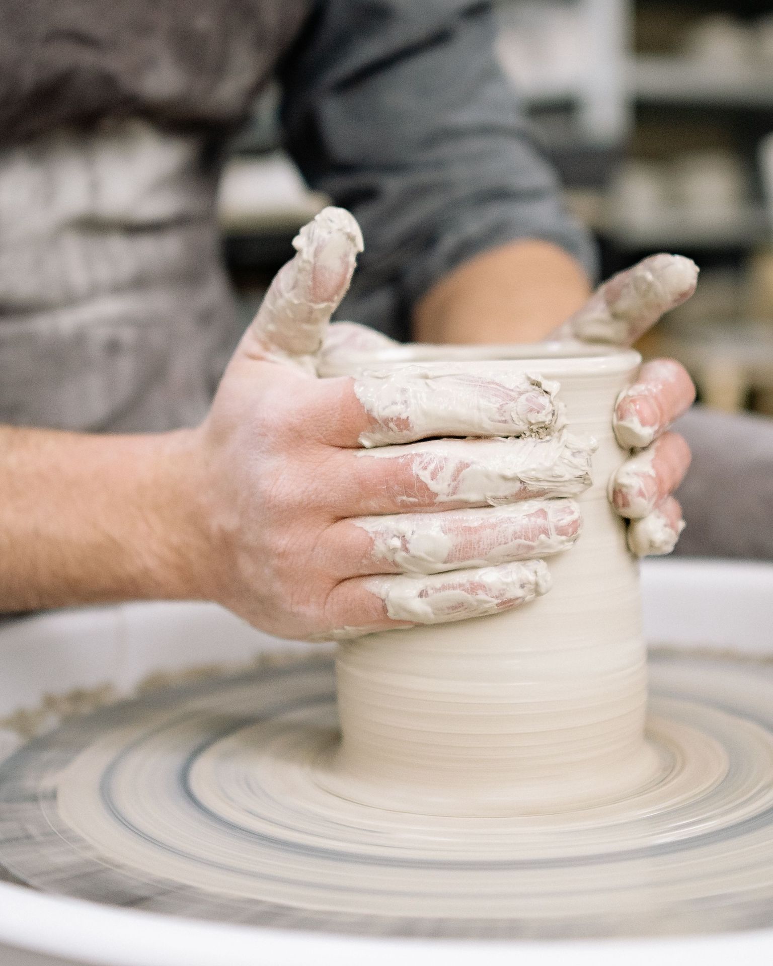 Hands pulling up a wet clay cylinder on the wheel.
