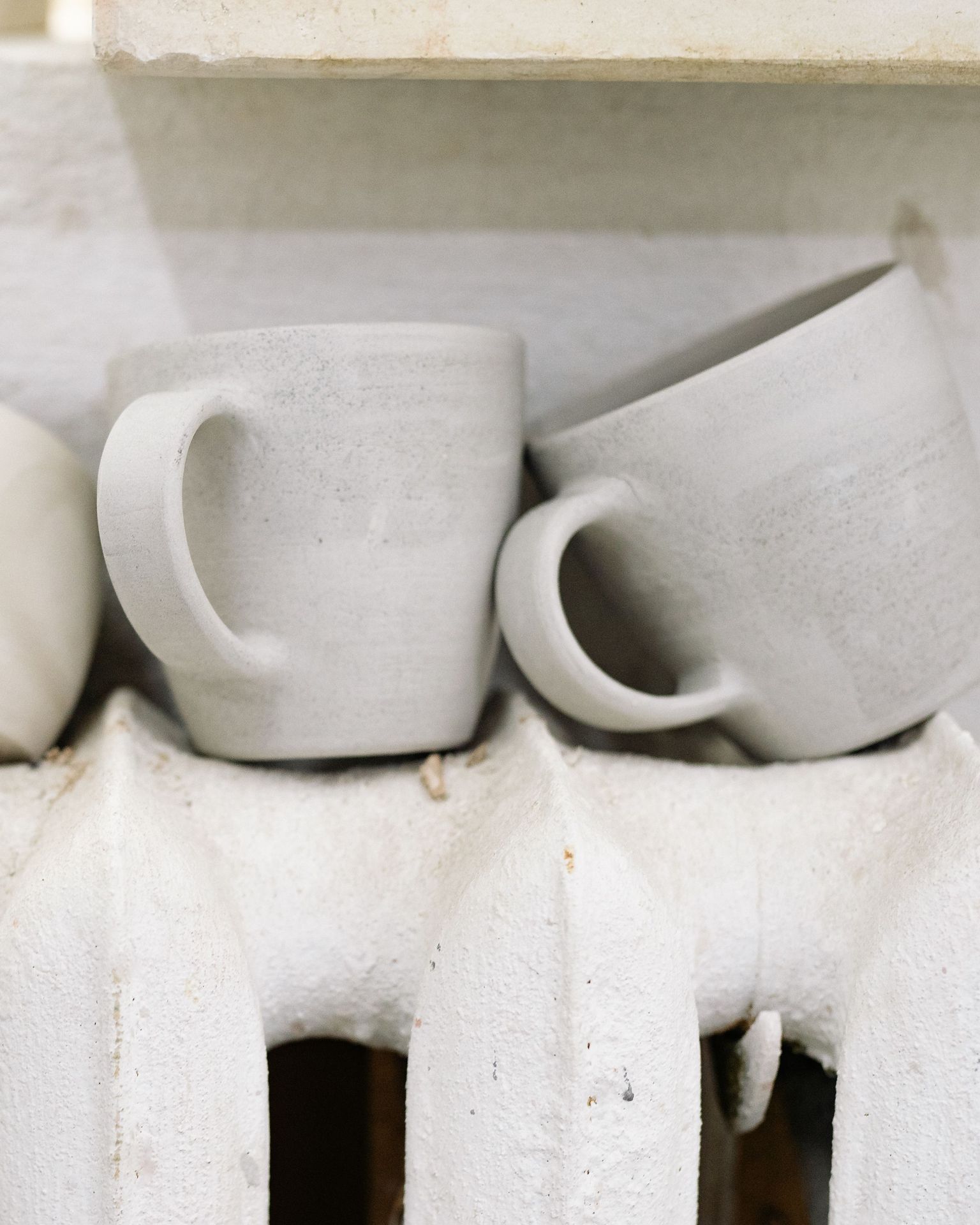 Leather-hard mugs with handles, drying on a radiator.